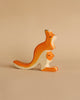 A small, wooden **Holztiger Kangaroo With Young** figurine handcrafted in Europe, featuring an adult kangaroo with a baby joey peeking out from its pouch. The figurine is painted in orange and white, typical of HOLZTIGER figures, and is set against a neutral beige background.