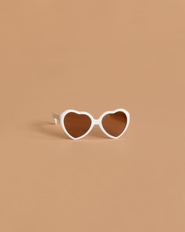 Minikane Doll Accessories | Loona Cream Heart Sunglasses: cream heart-shaped doll glasses with dark lenses, ideal for Minikane dolls, displayed on a solid light brown background.