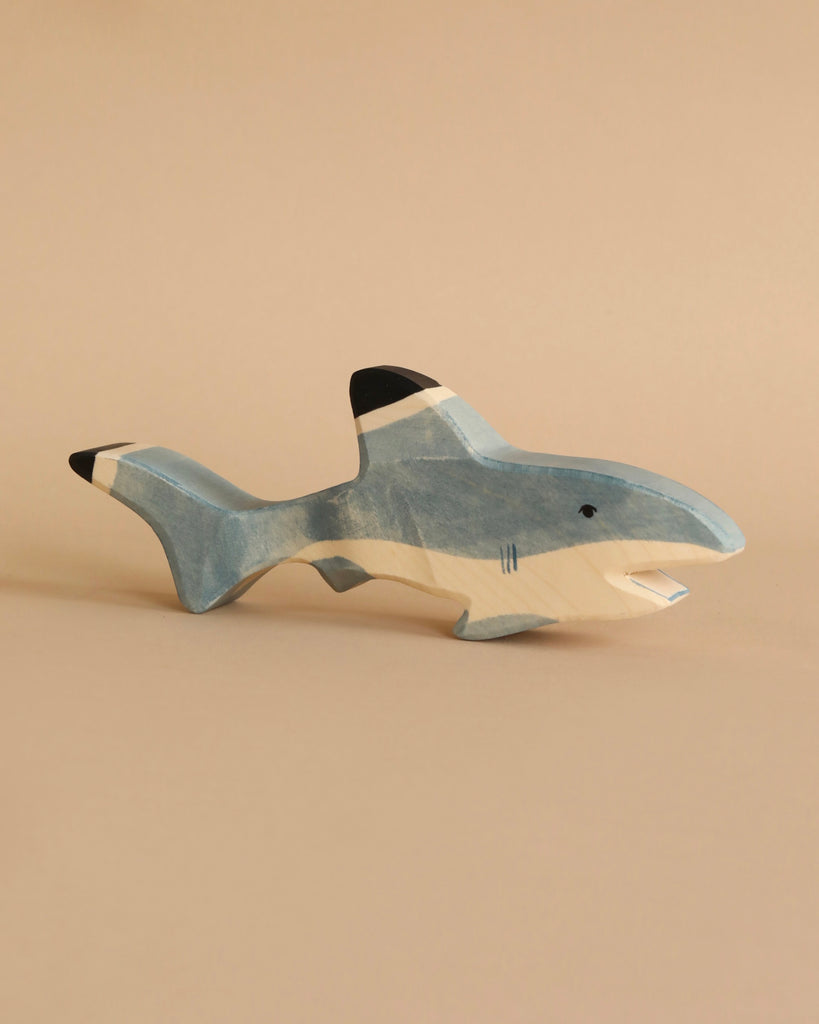 The Holztiger Handmade Wooden Sea Animals Set features a blue, white, and black shark figurine resting on a beige surface with a matching background, showcasing the charm of minimalist, handcrafted wooden toys.