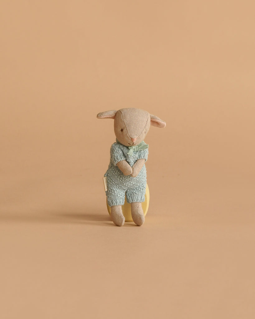 A Maileg Easter Egg with a plush lamb featuring magnetic hands and extra clothing sits upright against a plain, beige background.