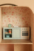 The Maileg Suitcasa Furnished Set features a miniature vintage kitchen with floral wallpaper, a small stove, oven, sink, and shelves displaying pastel-colored mugs, cans, and bowls—perfectly sized as Maileg mouse furniture or charming Maileg dollhouse accessories.