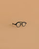 A pair of Minikane Doll Accessories Harry Sunglasses in black is centered on a plain, light brown background.