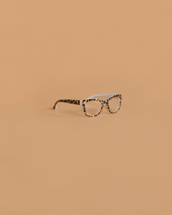 A pair of Minikane Doll Accessories | LEOPARD Doll Glasses with a stylish frame sits on a light brown background—perfect for accessorizing Minikane 13" dolls.
