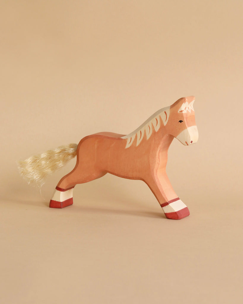 A Holztiger Handmade Wooden Horses Set toy featuring a handcrafted wooden horse with a painted tan body, white mane, and yarn tail.