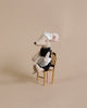 Maileg Maid Mouse classically made, wearing a black dress and light blue apron with a matching headscarf, discreetly equipped with magnets in hands for housekeeping tasks, sitting on a small, gold-colored chair against a plain beige background.