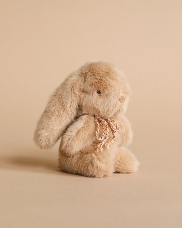 Mini plush bunny in cream peach color with bow. Photographed against beige background. 