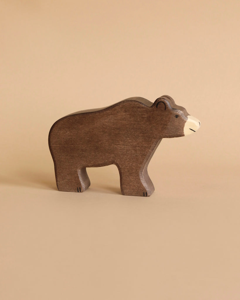 A simple, handcrafted wooden bear from the Holztiger Handmade Wooden Woodland Animals Set stands on a beige surface with a matching background—painted brown with a light snout, ideal for open-ended play and classic in style.