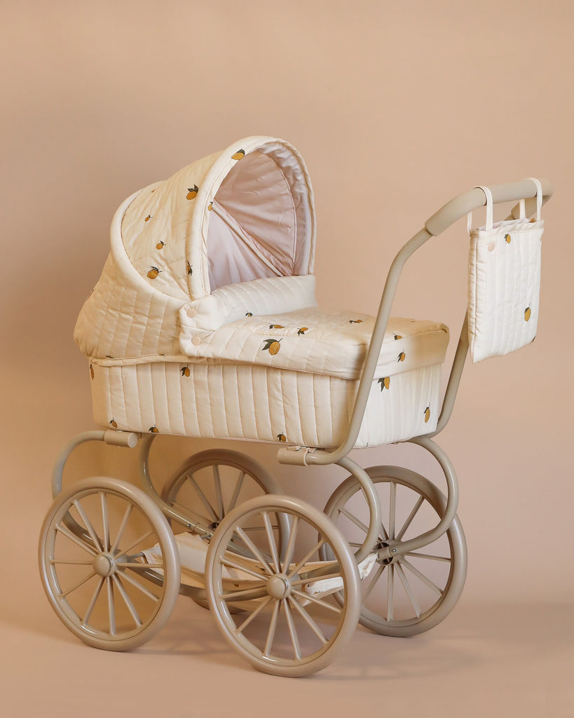 Introducing the Konges Sloejd Mini Doll Pram - Lemon, a vintage-style baby stroller adorned with cushioned quilted fabric and small gold patterns. It includes an attached bag and canopy and comes with a cushioned storage basket, all showcased against a plain light brown background.