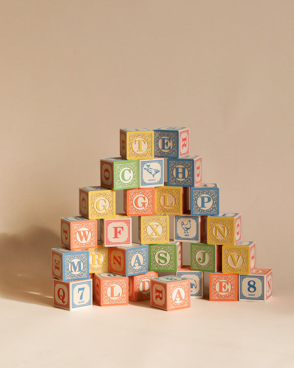 A pyramid of Uncle Goose Classic ABC Blocks neatly stacked against a light beige background, featuring a variety of letters and symbols in a playful font on wooden toys.