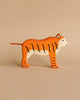 A handcrafted wooden Holztiger Handmade Wooden Safari Animals Set tiger with orange fur, black stripes, and a thin cord tail.