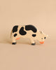 A Holztiger Grazing Black Cow with a natural finish and black spots stands against a beige background. Handcrafted in Europe by HOLZTIGER figures, the cow features an orange snout and black hooves, exuding charm and quality.