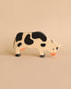 A Holztiger Handmade Wooden Black & White Cow Family Set figure with black spots, black hooves, and an orange muzzle, shown in a grazing position.