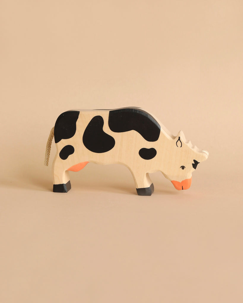 A Holztiger Handmade Wooden Black & White Cow Family Set figure with black spots, black hooves, and an orange muzzle, shown in a grazing position.