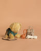 The Maileg Puppy Playtime Set with Goodie Bag features a plush puppy in a blue harness and leash, seated on a beige surface with a rope toy, "Goodie bag" tote, and rolled dog waste bag against a light brown background.