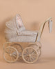 The Konges Sloejd Mini Doll Pram - Milk Tank is a vintage-style baby pram featuring quilted floral fabric, a large hood, and a matching bag that hangs on the handle. It has four large wheels and a light beige frame, complemented by a cushioned storage basket set against a plain background.