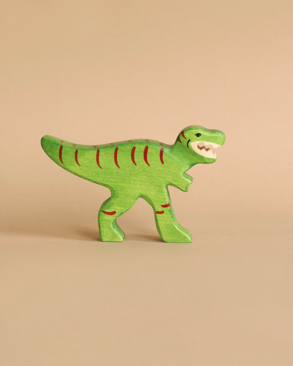 A small, green wooden Holztiger Tyrannosaurus Rex Dinosaur with red stripes and an open-mouthed expression is standing on a beige background. Handcrafted wood gives it a simplified, cartoonish design, reminiscent of HOLZTIGER figures and proudly made in Europe.