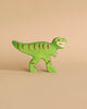 A small, green wooden Holztiger Tyrannosaurus Rex Dinosaur with red stripes and an open-mouthed expression is standing on a beige background. Handcrafted wood gives it a simplified, cartoonish design, reminiscent of HOLZTIGER figures and proudly made in Europe.