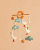 Handmade Mobile - The Sleepy Goose - Final Sale features felt ducks, clouds, stars, balls, and a crescent moon delicately hanging from a wooden hoop against a peach background. This charming nursery mobile adds a whimsical touch to any room.