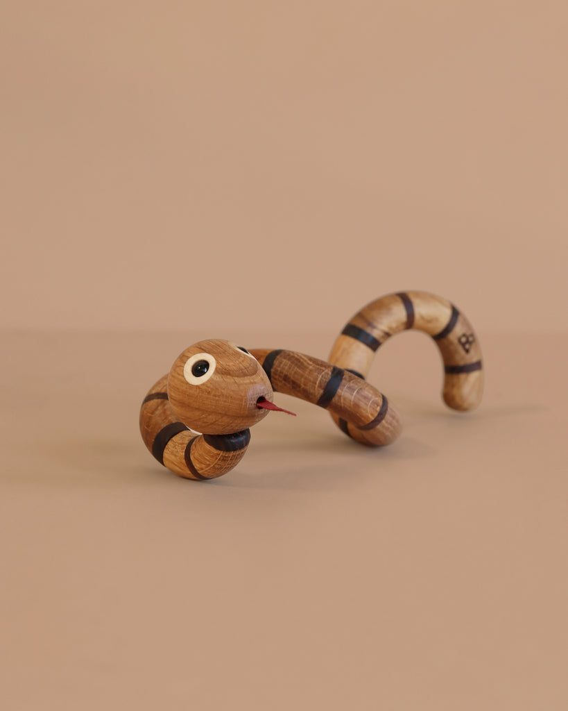 Spring Copenhagen The Snake, featuring black stripes, movable segments, googly eyes, and a red tongue, is posed on a plain beige background—making it a charming piece of wooden décor inspired by the Chinese zodiac snake.