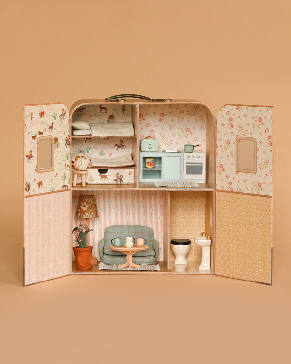 The Maileg Fully Furnished SuitCasa is a small, open mouse house with floral wallpaper, featuring bunk beds in the bedroom, kitchen accessories by the stove and shelves, a living room with blue sofa and table, plus a bathroom with toilet and sink.