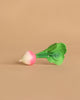 Ramona the Radish Teething Toy, featuring green leaves and a white-and-pink root, rests on a plain beige background—an ideal natural rubber baby toy for sensory play.