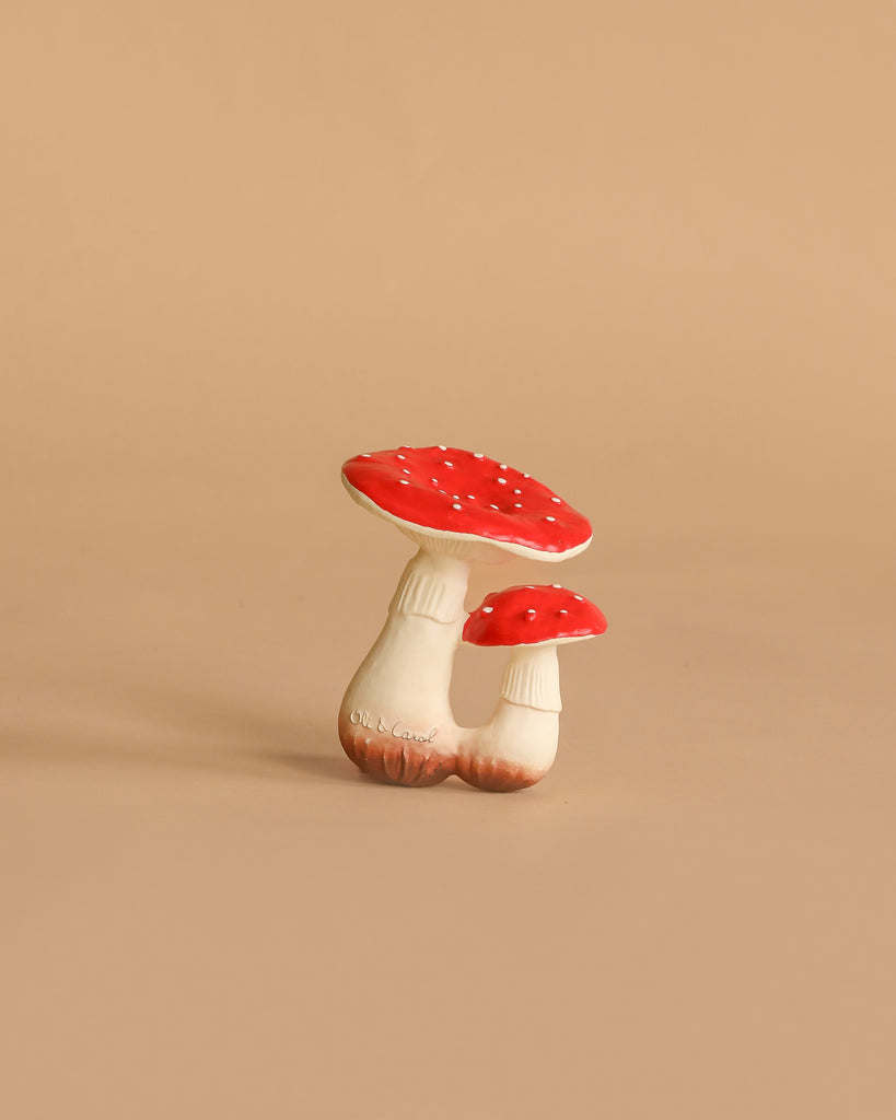 The Spot the Mushroom Teething Toy features two red-and-white mushrooms with white stems, connected at the base and set against a plain beige background—perfect for whimsical sensory play.