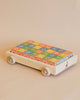 A handmade basswood wagon with four wheels carries the Uncle Goose Classic ABC Blocks with Wagon. The blocks feature letters, numbers, and decorative designs in blue, red, yellow, and green. The charming cart and its vibrant contents rest against a beige background.