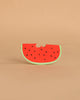 Wally the Watermelon Teething Toy, made from natural rubber with a green rind, red flesh, and black seeds, is perfect for safe teething or sensory play. It’s shown against a plain beige background as a bright, semicircular slice.