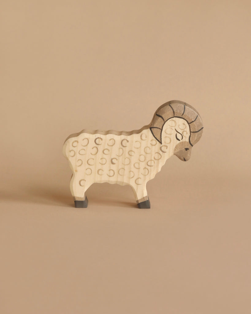 A small wooden toy resembling a ram stands on a neutral beige background. The Holztiger Ram features carved details, including a textured body, curved horns, and gray hooves. Its simple, minimalist design creates a charming appearance typical of handcrafted wood toys made in Europe.