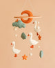 Introducing the Handmade Mobile - The Sleepy Goose (Final Sale): a delightful handmade baby mobile adorned with felt ducks, stars, clouds, and a crescent moon. Gracefully suspended against a peach backdrop, this decorative ceiling mobile features soothing shades of soft orange, white, and teal—making it the perfect nursery accent to bring whimsical charm and gentle comfort to your little one’s space.