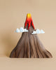 The Bumbu Handmade Wooden Prehistoric Set features a wooden volcano model with red and yellow lava, two white cloud cutouts, and non-toxic paint—ideal for imaginative play or as a display piece. Shown against a beige background.