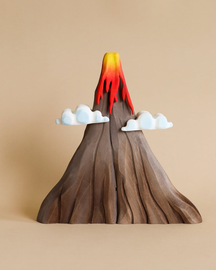 The Bumbu Handmade Wooden Prehistoric Set features a wooden volcano model with red and yellow lava, two white cloud cutouts, and non-toxic paint—ideal for imaginative play or as a display piece. Shown against a beige background.
