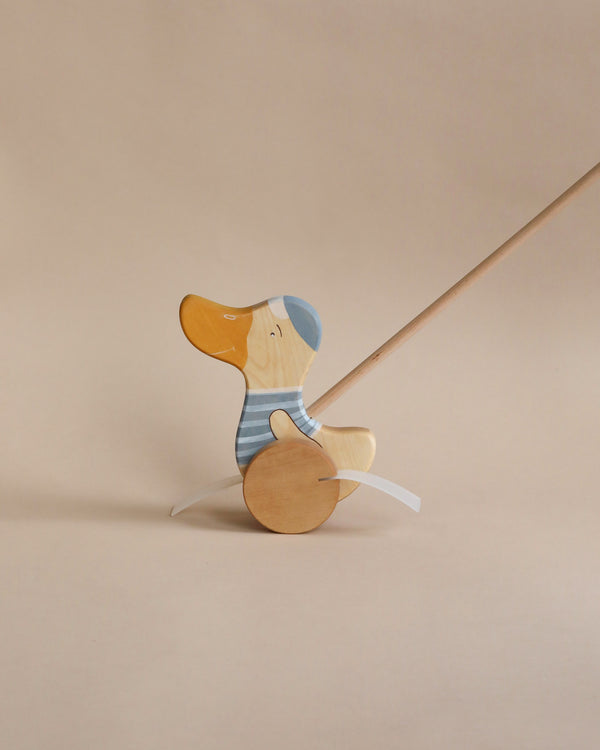 A Handmade Wooden Duck Push Toy, crafted from sustainably harvested birch wood and painted with natural milk paint in light blue and yellow hues, impaled by a thin metal rod against