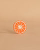 A single round slice of orange grapefruit with a white rind sits upright on a light beige background, echoing the design of Clementino the Orange Teething Toy—a natural rubber baby toy for teething and sensory play.