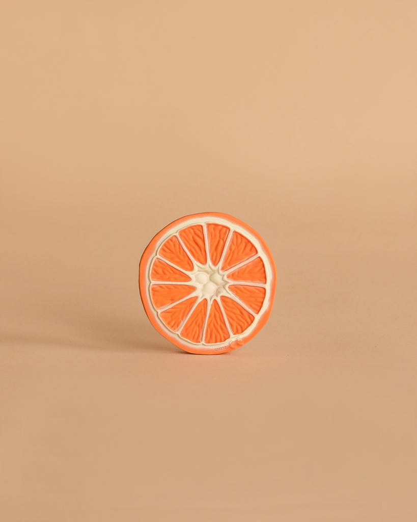 A single round slice of orange grapefruit with a white rind sits upright on a light beige background, echoing the design of Clementino the Orange Teething Toy—a natural rubber baby toy for teething and sensory play.