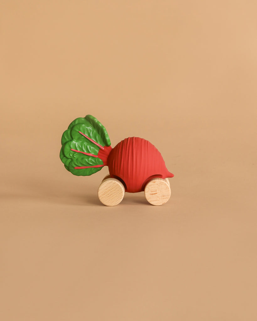 Betty The Beetroot Baby Car, an eco-friendly toy with a red beetroot shape, green leaves, and four wooden wheels, is shown on a plain beige background.