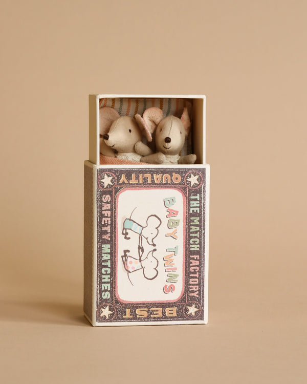 Two small Maileg Twin Baby Mice In Matchbox toys peeking out of a decorated matchbox with vintage style design, labeled "the matchbox baby twins" against a neutral backdrop.