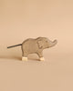 From the Holztiger Handmade Wooden Safari Animals Set, a light brown wooden elephant toy with white feet, a painted smile, and a dark cord tail stands against a beige background in simple, minimalist style.