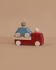 The Lubulona Wooden Tow Truck - Red, featuring a minimalist design with a red body, light wood wheels, and two peg people—one blue and one natural—invites small-world play on a plain beige background.