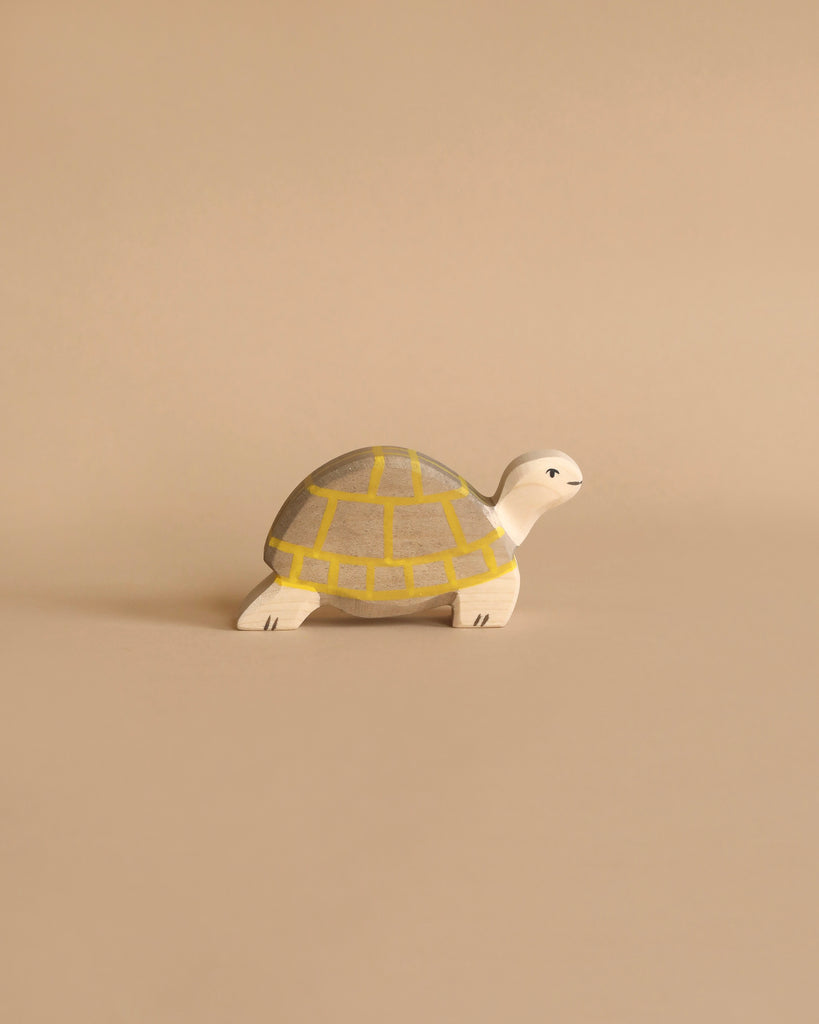 A small wooden turtle with a yellow and gray shell stands on a beige surface, blending with the background—part of the charming Holztiger Handmade Wooden Ocean Animals Set for fans of handcrafted toys.