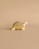 The Holztiger Handmade Wooden Sea Animals Set includes a maple and beech wood turtle figurine with a yellow and gray shell, displayed on a beige surface that matches its charming artisanal style.