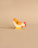 A small, hand-painted chicken from the Holztiger Handmade Wooden Animal Play Set, featuring a yellow body, red comb, and orange accents, stands on a beige background—highlighting European craftsmanship.