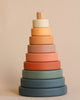 A Wooden Pyramid Stacker - Green & Mustard with a central vertical peg and seven chunky rings in a gradient of earth tones, arranged from largest at the bottom to smallest at the top, coated in non-toxic paint.