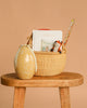 The Easter Basket Gift Set, featuring a Farmers Market board book, plush fox toy, and pencil in a basket on a wooden stool beside a Maileg Easter Egg, is displayed against a beige background.