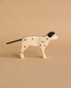 A Holztiger Handmade Wooden Farm Animals Set toy dog, featuring a white body with black spots, ear, and tail, crafted from maple and beech wood, is displayed on a beige background.