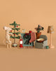 The Maileg Little Sister Cozy Christmas Living Room Set features a mouse decorating a mini Christmas tree beside a checked armchair, side table, clock, lantern, cup, floor lamp, and accessories, all on a warm beige background.