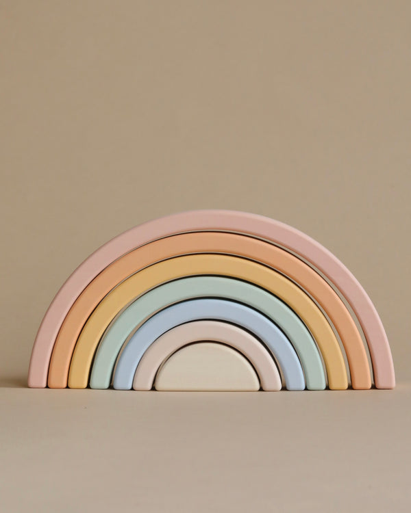 A Handmade Rainbow Stacker - Pastel with soft pastel shades of pink, peach, blue, and cream arranged in ascending arches against a plain beige background.