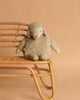 The Senger Naturwelt Cuddly Animal - Linen Sheep, a plush beige lamb with closed eyes and floppy ears, sits on a rattan bench against a light brown background, exuding calm and relaxation.