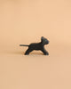 A small, black wooden figurine of a panther stands against a neutral beige background. Handcrafted from wood and Made in Europe, the Holztiger Panther, Small features simple painted details like white lines for ears, eyes, and mouth, alongside a grey tail. Its minimalist design captures the panther's playful posture perfectly.