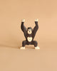 A dark brown and beige wooden gorilla toy from the Holztiger Handmade Wooden Safari Animals Set stands with both arms raised against a plain beige background, highlighting the charm and craftsmanship of these handmade safari animals.